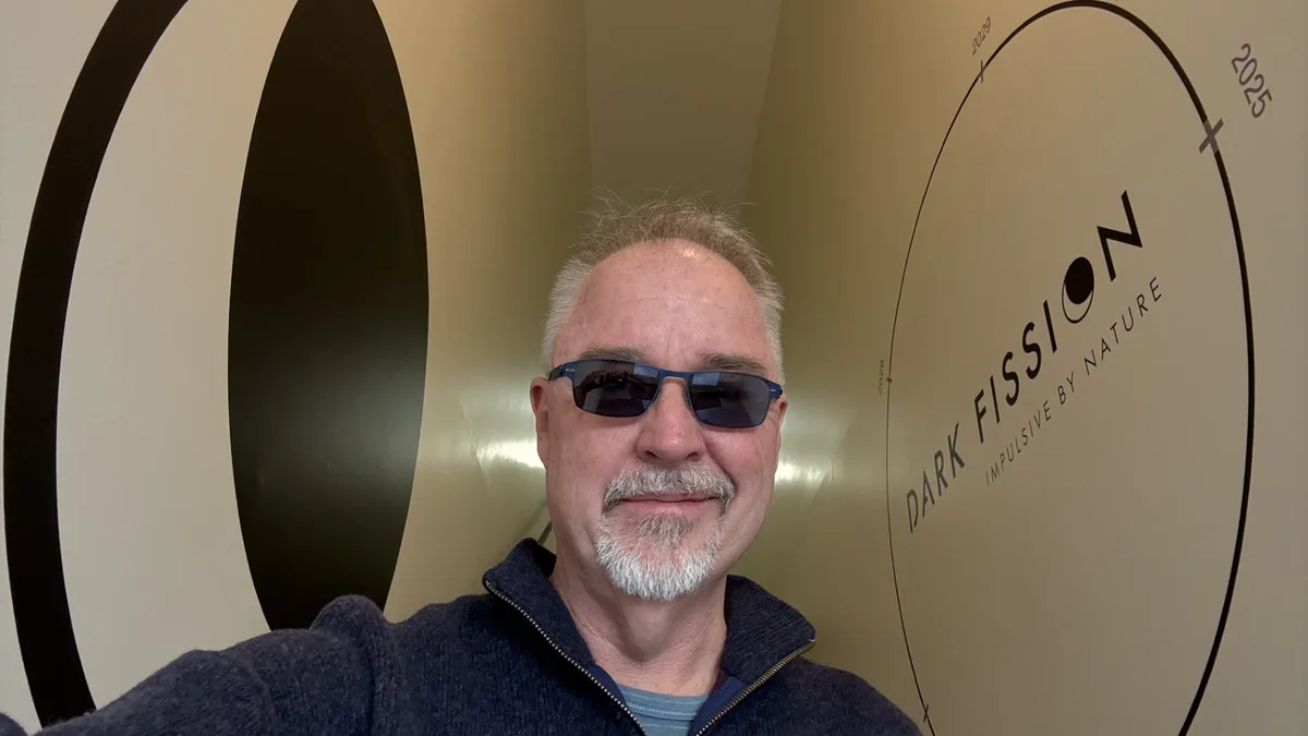 Dark Fission CEO Fred Kennedy in the Liberty Street office hallway, in front of a wall-sized Dark Fission logo with a program timeline running 2025 through 2029