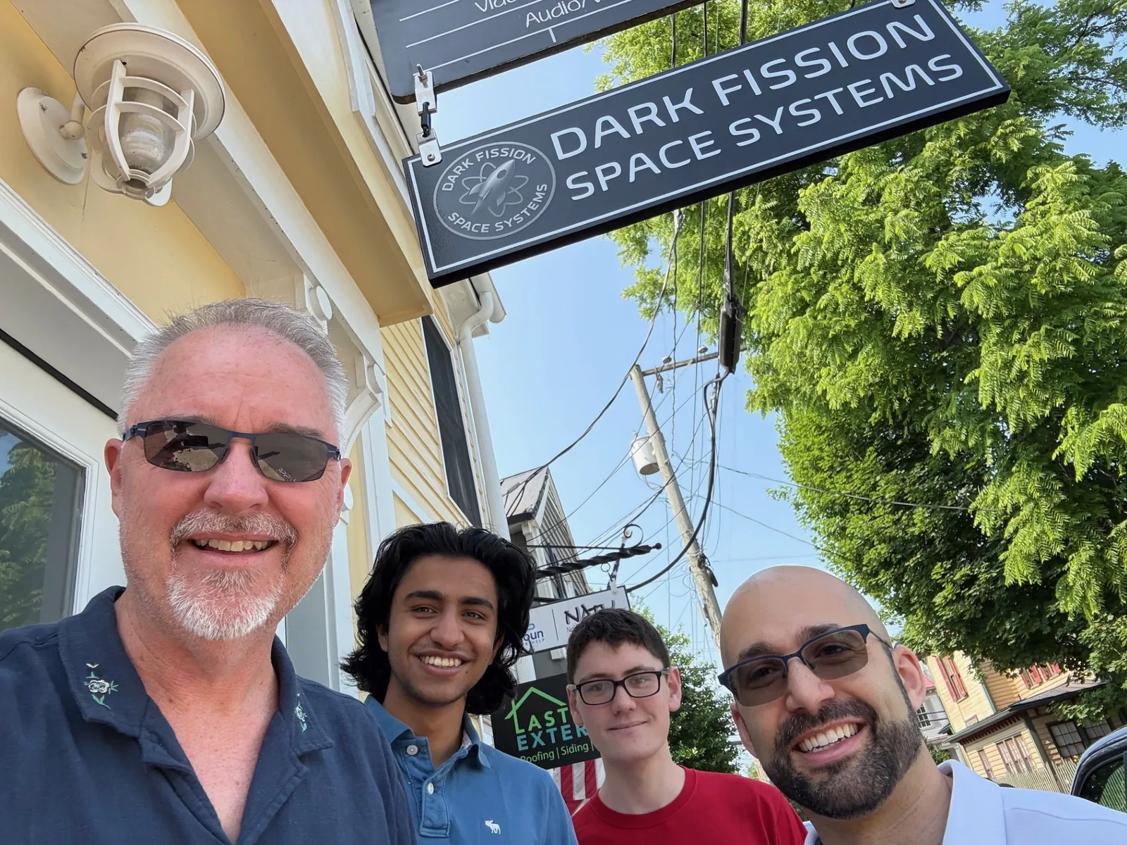 Four Dark Fission team members under the Dark Fission Space Systems sign outside the Liberty Street office in Leesburg, Virginia